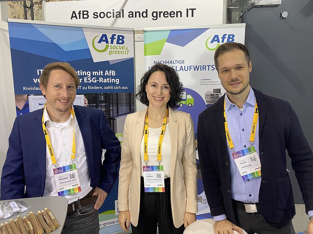 Three employees of AfB standing in front two advertising posters presenting the services and supplies of AfB at the exhibition area of the 57th symposium procurement and logistics at STATION in Berlin.
