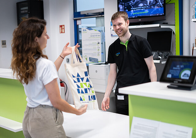 AfB-Mitarbeiter übergibt Kundin ihren Einkauf in einer nachhaltigen AfB-Tasche.