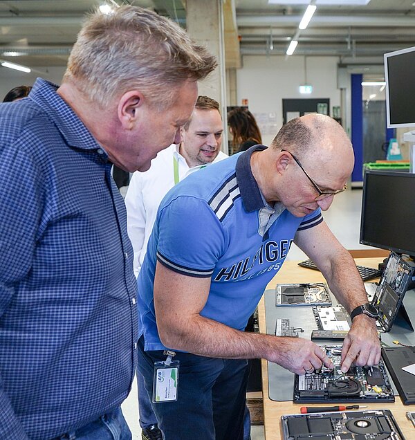 Drei Besucher von Bertelsmann versuchen sich an einer Refurbishment-Challenge. Sie dürfen kleinere Reparaturen an Laptops mit unterschiedlich guter Reparierbarkeit durchführen. Die Herren sind Dirk Kunz, Achim Bernsmann und Christian Rauch.