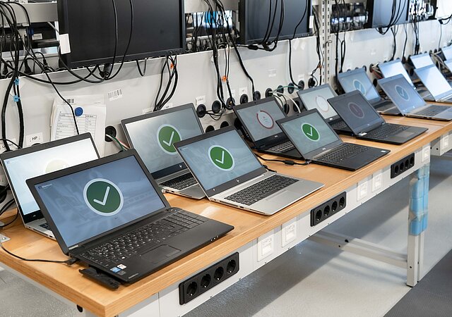 Eine Reihe Laptops mit grünem Haken auf dem Display steht auf einer Werkbank.