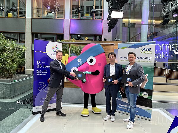 drei Männer und das Maskottchen von Special Olympics stehen im ZDF-Hauptstadtstudio mit Laptops von AfB in der Hand