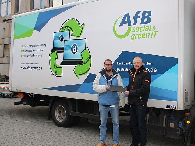 2 men in ski jackets stand in front of an AfB truck with a laptop in their hands.
