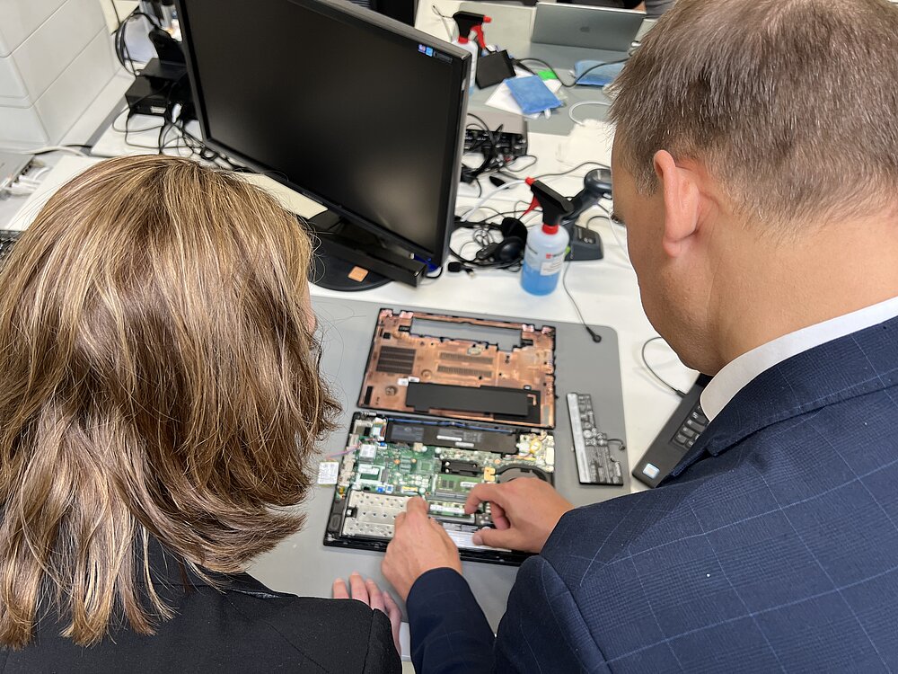 Zwei Personen arbeiten an einem aufgeschraubten Laptop
