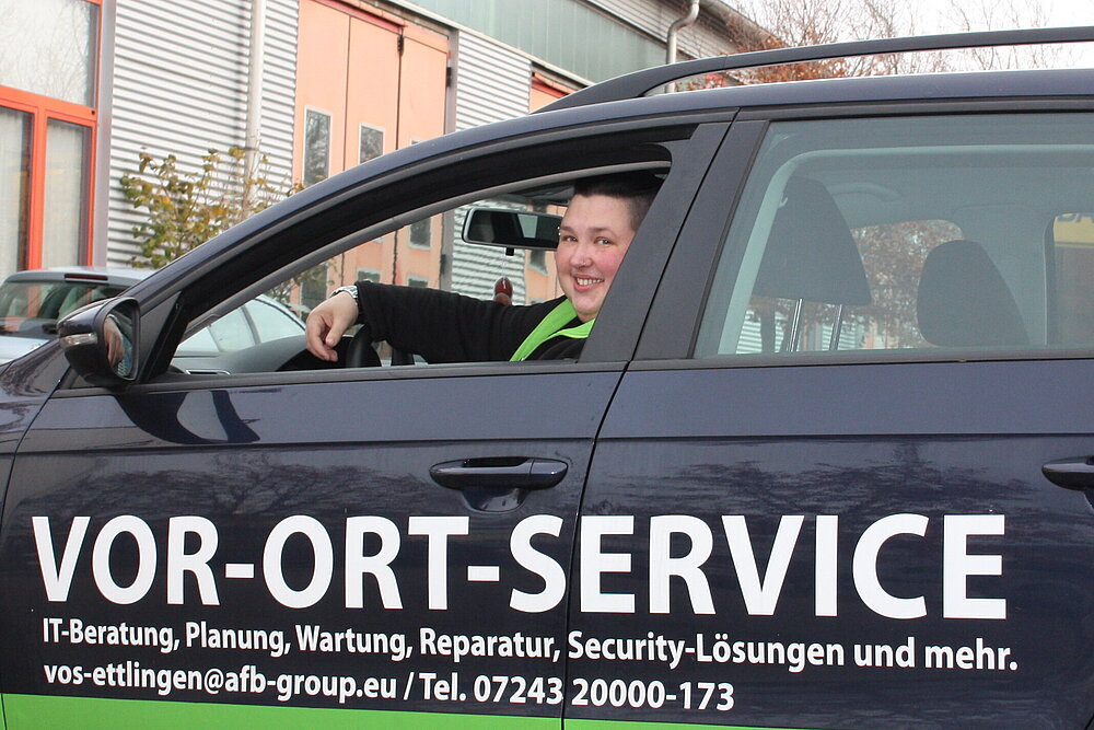 AfB Mitarbeiterin des VOR-ORT-SERVICE im Wagen lenkend und lächelnd / Fuhrpark der AfB / Logo social & green IT