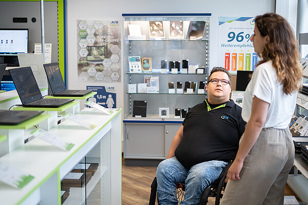 AfB-Shop Mitarbeiter im Rollstuhl berät Kundin zu refurbished Notebooks.