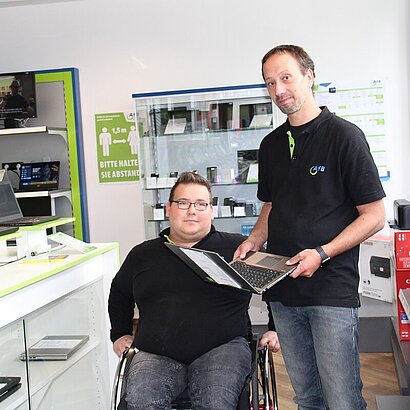 Zwei Mitarbeiter im AfB-Shop präsentieren ein refurbishtes Notebook