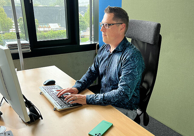 Dominik Gomer, Head of E-Commerce bei AfB social & green IT, sitzt im Büro an seinem Schreibtisch, neben ihm das Fairphone 4. 