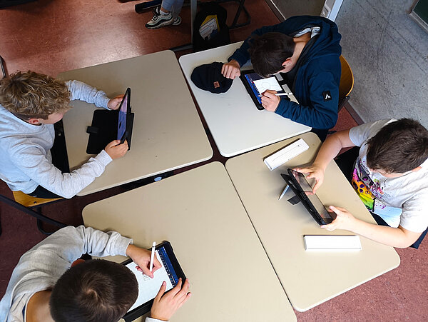 Aufnahme aus der Vogelperspektive, vier Schüler:innen arbeiten in der Schule an ihren iPads.