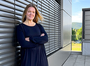 Sustainability Managerin Agnes Strehle lehnt in einem dunkelblauen Kleid an einer Wand.