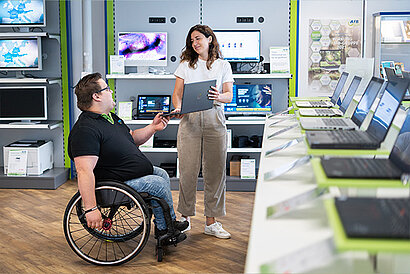 An employee in a wheelchair advises a customer on the purchase of a refurbished notebook.