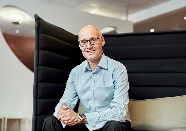 CEO von Apollo Jörg Ehmer sitzt auf einem Sessel und lächelt in die Kamera