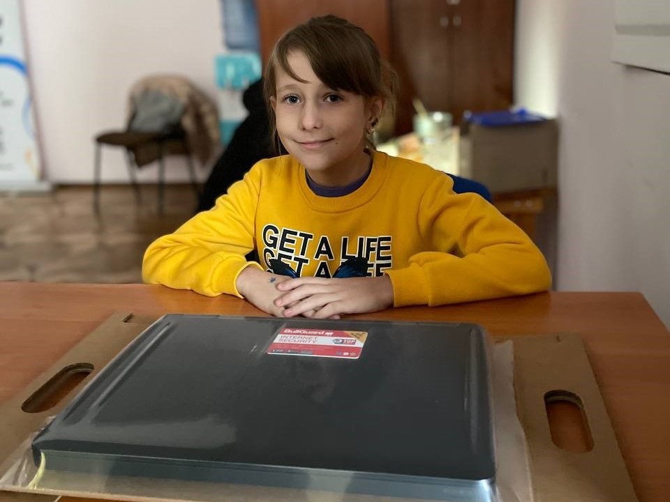 Ein jungen Mädchen sitzt freudestahlend an einem Tisch, vor ihr liegt ein eingepacktes Notebook von AfB