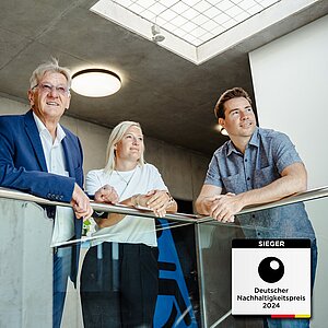 2 Männer und eine Frau lehnen an einem Geländer und blicken in eine Richtung. In der rechten unteren Ecke befindet sich das Sieger-Siegel für den deutschen Nachhaltigkeitspreis 2024.